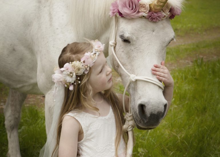 Girl in dress looking up and whispering to a magical unicorn