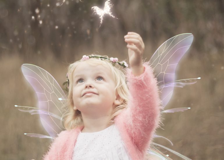 Girl reaching towards butterflies flying in fantasy photo shoot